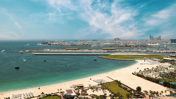 Um resort costeiro com praia, marina e o horizonte urbano ao fundo.