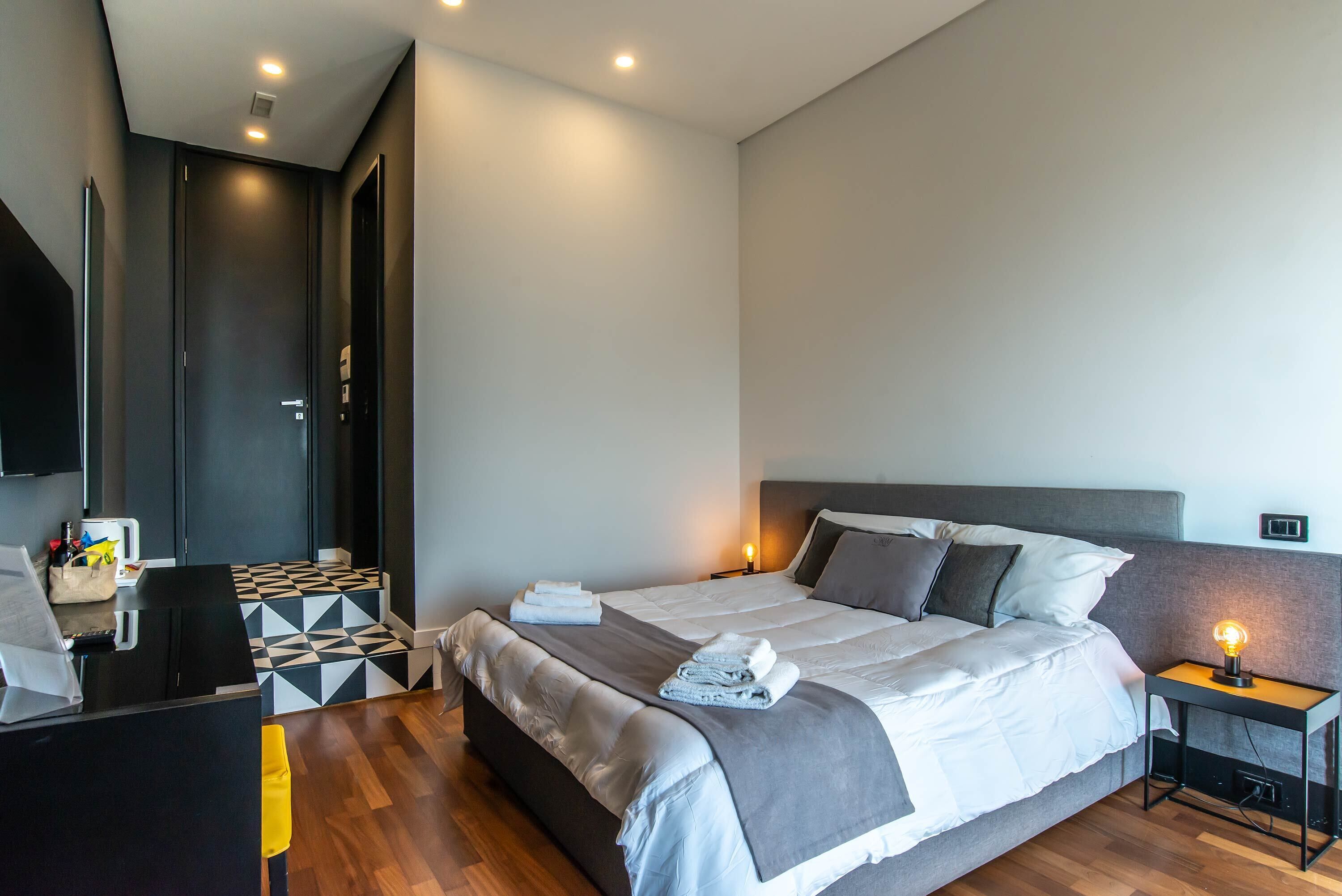 Quarto de hotel moderno com uma cama grande, uma escrivaninha e uma televisão.