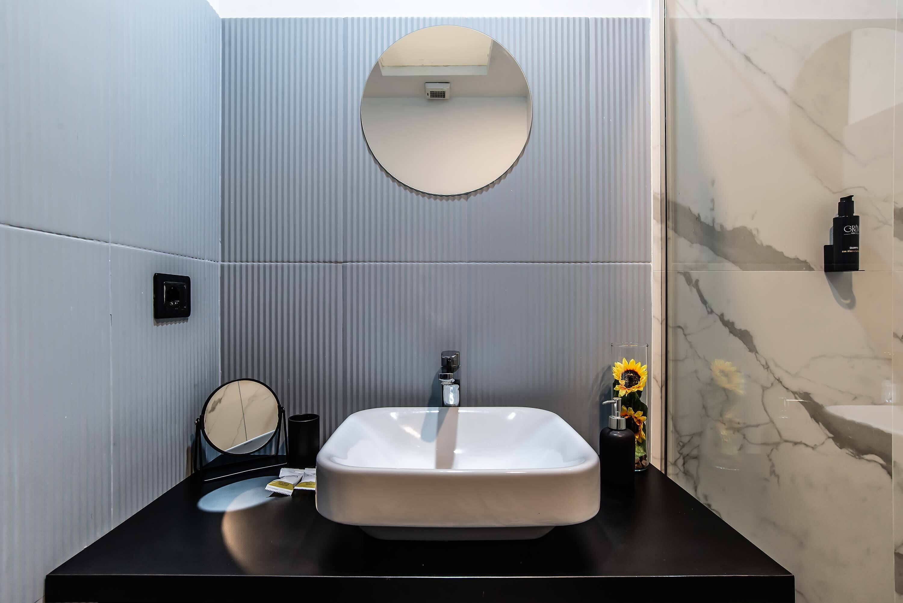 A bathroom with a white sink, a round mirror, and a marble wall.