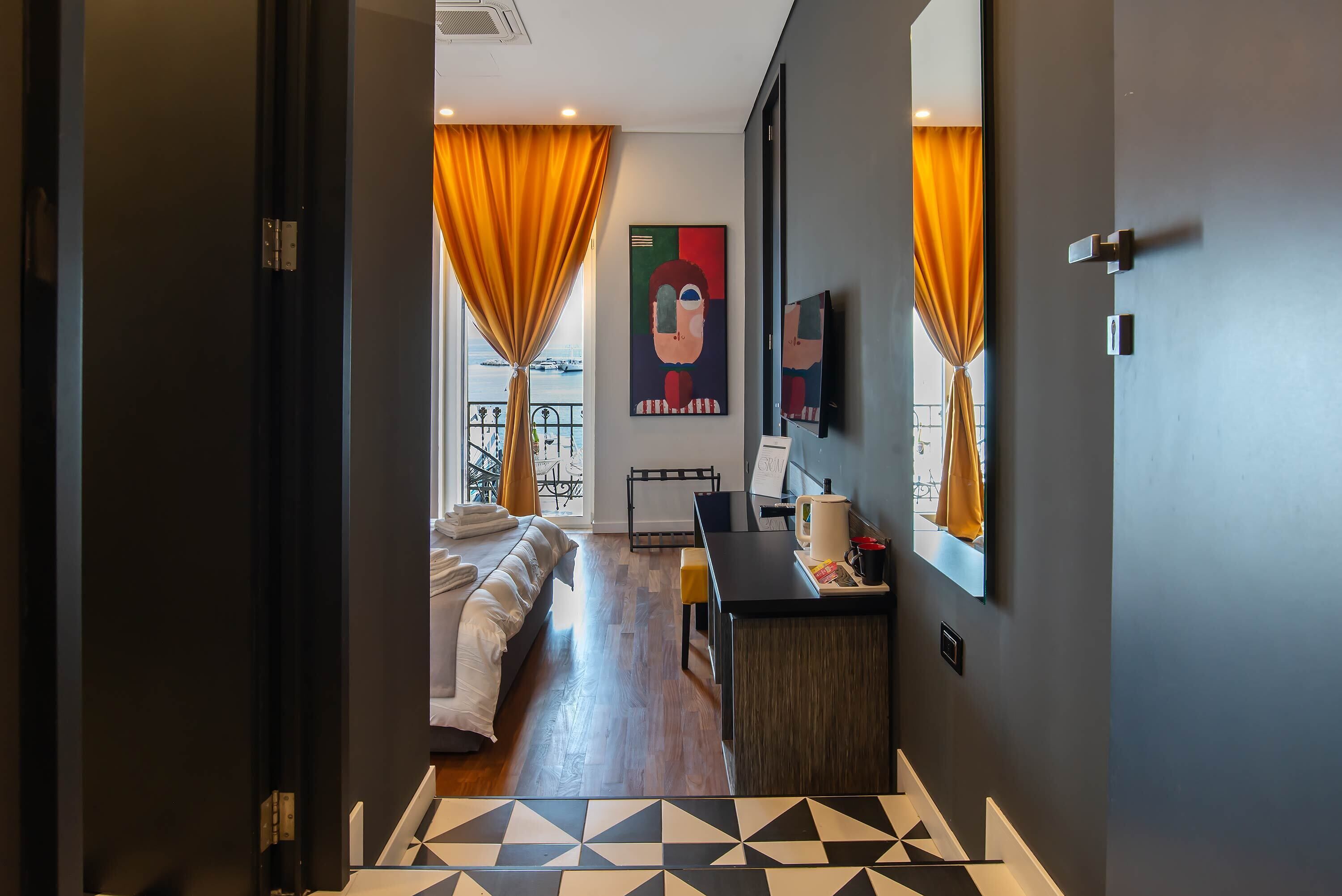 A modern hotel room with a bed, a desk, a chair, and a large window with curtains.