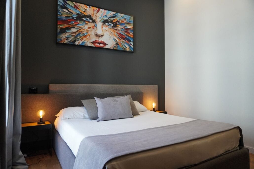 Un dormitorio moderno con una cama grande, dos mesitas de noche con lámparas, un cabecero y un cuadro abstracto colorido en la pared.