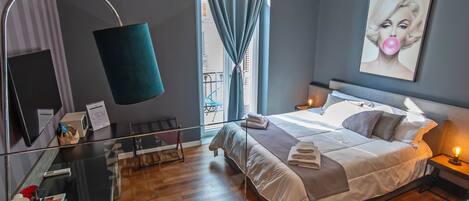 Un dormitorio moderno con una cama grande, un escritorio con computadora, un espejo y una ventana con cortinas.