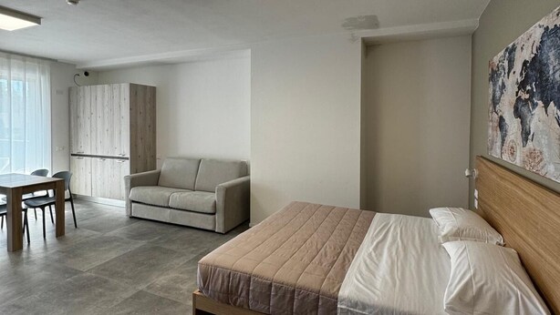 A modern bedroom with a large bed, a sofa, a dining table, and a view of the outside. - Dormi-RE (Reggio nell'Emilia)