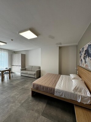 Un dormitorio moderno con una cama grande, un sofá, una mesa de comedor y vistas al exterior.