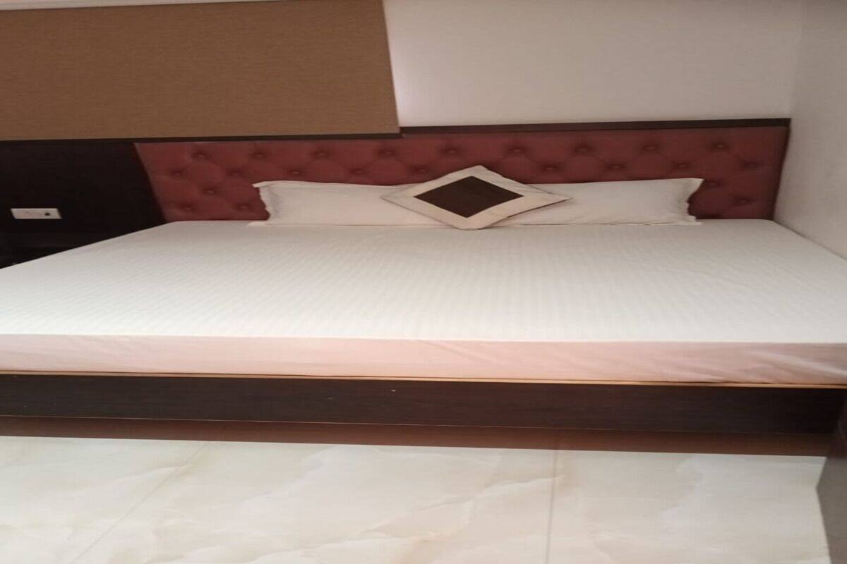 Una cama con estructura de madera, cabecera tapizada en rojo y dos almohadas.