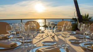 Een tafel gedekt voor een maaltijd, met uitzicht op de oceaan tijdens zonsondergang.