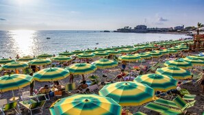 Een strand met veel groene en gele parasols, ligbedden en mensen die ontspannen.