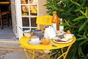 A yellow table set with breakfast items including a mug, a glass of orange juice, a plate with fruits and nuts, a bottle, and a teapot. - Hotel Marie Eder (Arcangues)