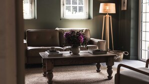 Ein gemütliches Wohnzimmer mit Ledersofa, Couchtisch mit Blumenvase, Stehlampe und Fenster mit Tageslicht.
