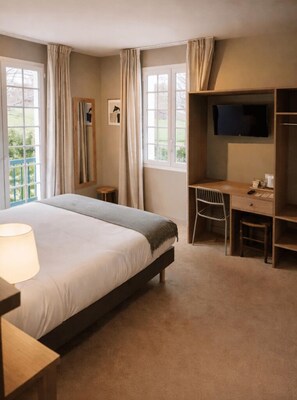 A hotel room with a bed, a desk, a chair, a TV, and large windows. - Hotel Marie Eder (Arcangues)