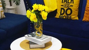 A round white table with a yellow stool, a vase with yellow flowers, and a book titled 'CHANEL' on the table. - Lux Suites Rosavosa Apartments Bamburi (Mombasa)