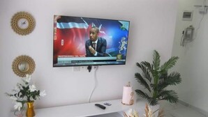 A television mounted on a wall displaying a news broadcast. - Lux Suites Rosavosa Apartments Bamburi (Mombasa)