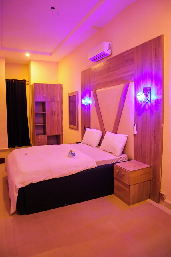 A bedroom with a large bed, wooden headboard, and built-in wardrobe. - La Villa (Awka)