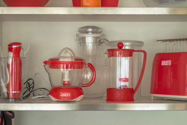 A kitchen shelf with various red kitchen appliances, including a blender, a juicer, and a coffee maker.