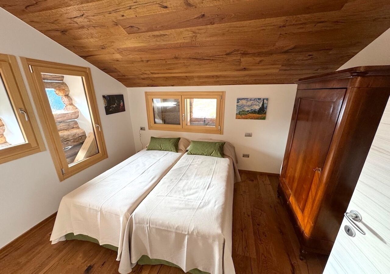 Een slaapkamer met een houten plafond, twee bedden met witte lakens, een houten kast en een raam met uitzicht.