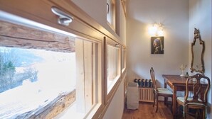 A narrow room with a wooden floor, a radiator, a table with chairs, and a window with a view of a snowy landscape.