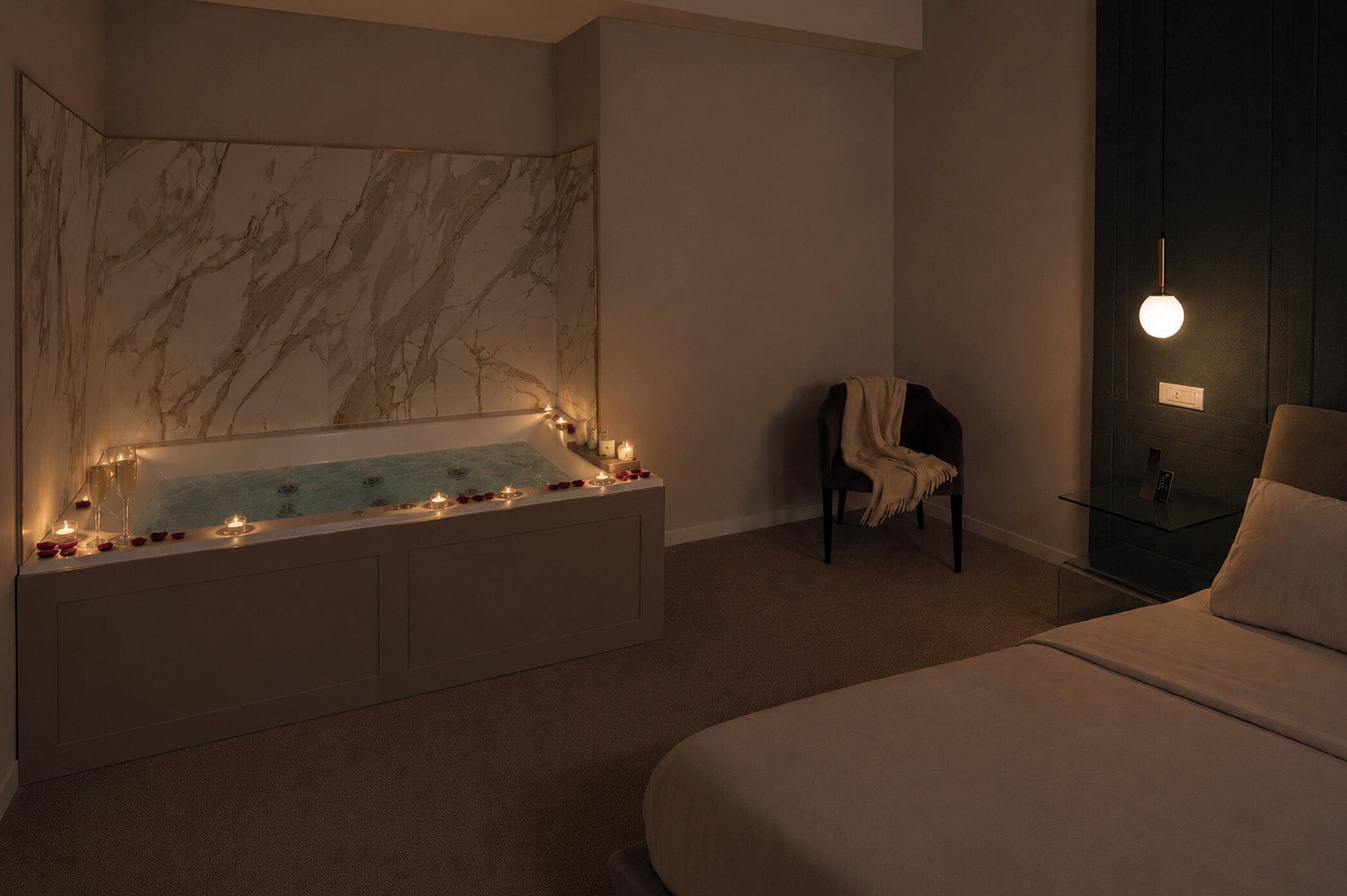 Ein modernes Badezimmer mit Marmorwand, einer Badewanne und einem Nachttisch mit Lampe.