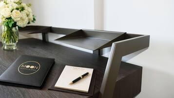 A desk with a black leather-bound notebook, a pen, and a glass vase with white flowers.