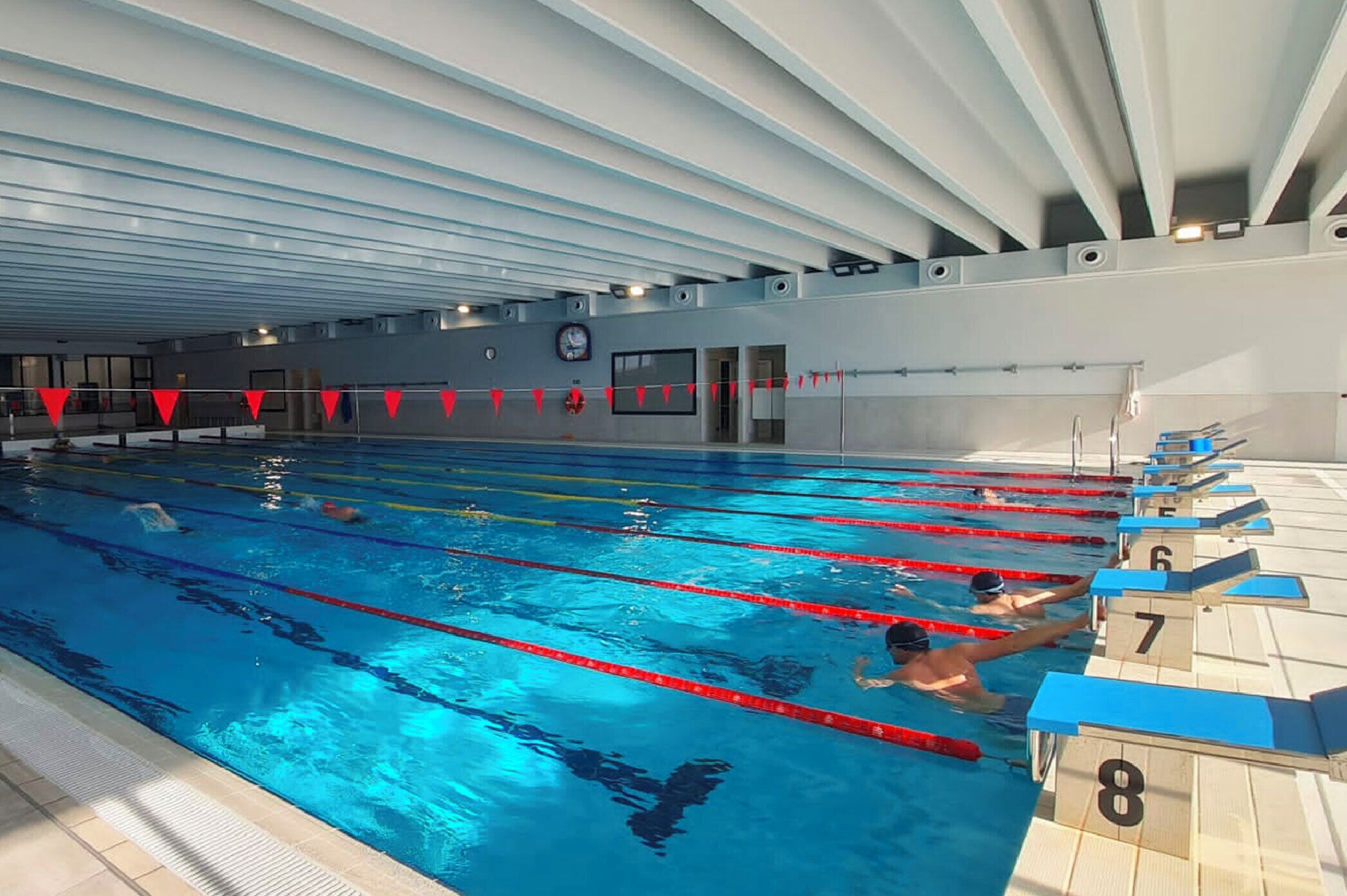 An indoor swimming pool with lanes, a clock, and numbered starting blocks.