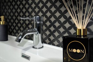 A modern bathroom with a chrome faucet, a black and gold bottle of Moon fragrance, and a black candle holder. - Moon Resort & Spa (Isernia)
