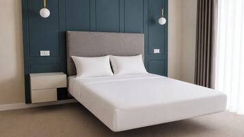 Una cama con cabecera gris, ropa de cama blanca y dos mesitas de noche con lámparas.