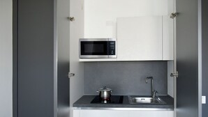 Een kleine keuken met een magnetron, kookplaat en spoelbak.