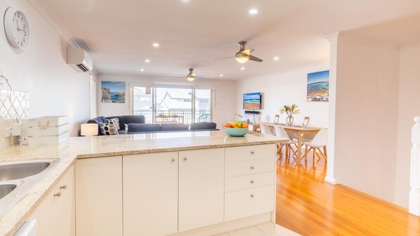 A modern kitchen with a central island, a dining area with a wooden table and chairs, and a view of the sea through large windows.