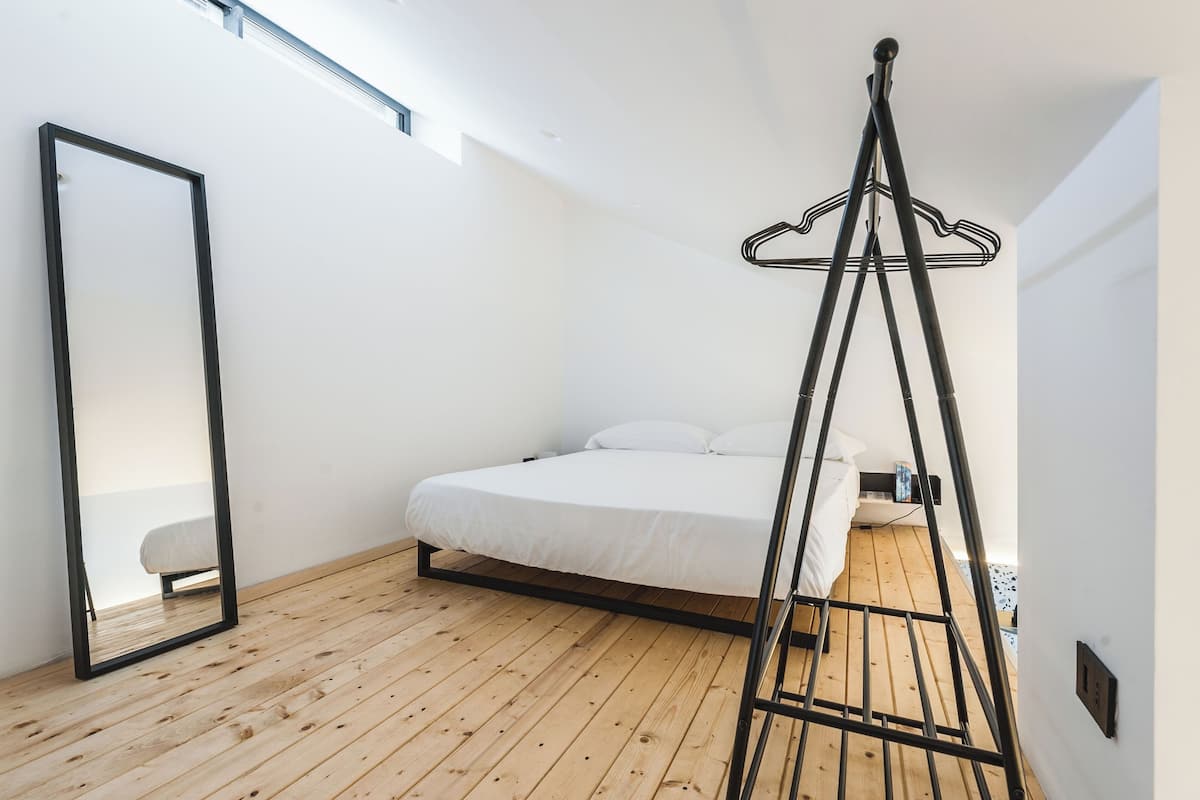 Une chambre à coucher avec un lit, un fauteuil suspendu, un miroir et un plancher en bois.