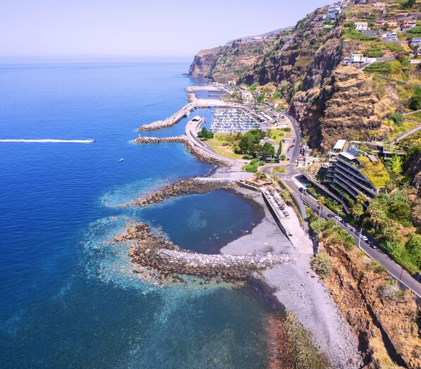 A coastal town with a marina, rocky shoreline, and buildings on a hillside. - Room-discover Magical Calheta (Calheta)