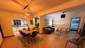 A spacious living area with a dining table, sofa, and chairs, connected to a kitchen and a bedroom.