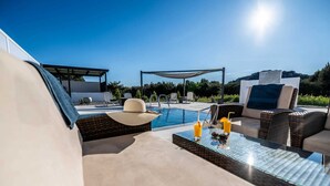 Zona de piscina con sillones reclinables, una mesa con bebidas y vista al estanque.