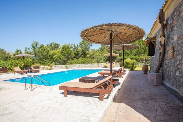 A pool area with lounge chairs, umbrellas, and a stone building. - illa in the Woods is a stunning stone-and-wood property in Kolympia area. (Kolymbia, Rhodes)