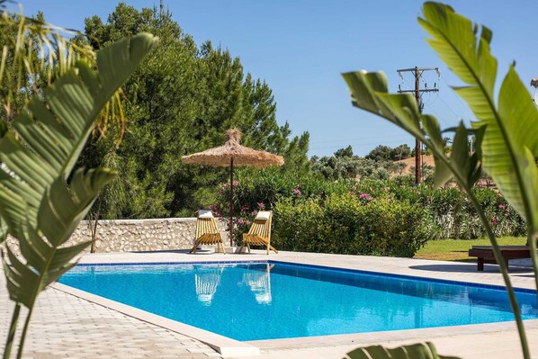 Una piscina con due lettini di legno e un ombrellone di paglia.