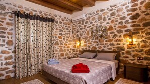Un dormitorio con pared de piedra, una cama con toalla roja y dos luces fijadas a la pared.