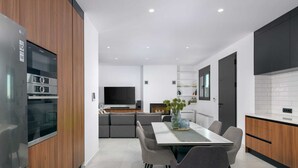 Una cocina moderna con electrodomésticos integrados, un comedor con mesa y sillas, y un televisor al fondo.