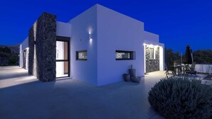 Una casa moderna con un pilar de piedra, un patio con mobiliario exterior y una entrada bien iluminada.