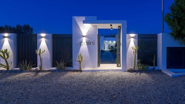 Entrada moderna a una villa con camino de grava, cactus y un sendero bien iluminado que conduce al interior.