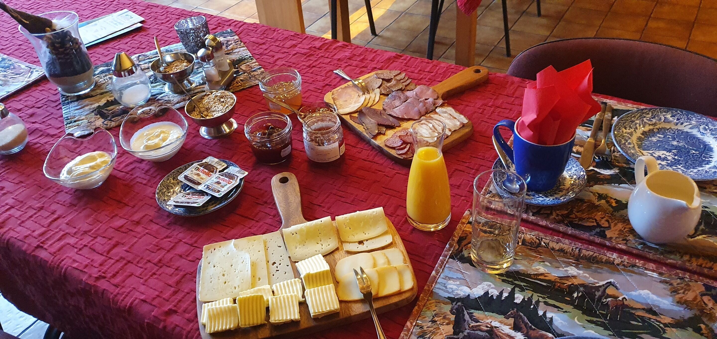 A table set with various food items, including cheeses, meats, and condiments, on a red tablecloth.