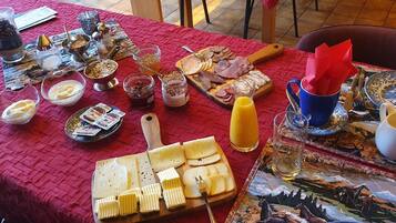 A table set with various food items, including cheeses, meats, and condiments, on a red tablecloth.