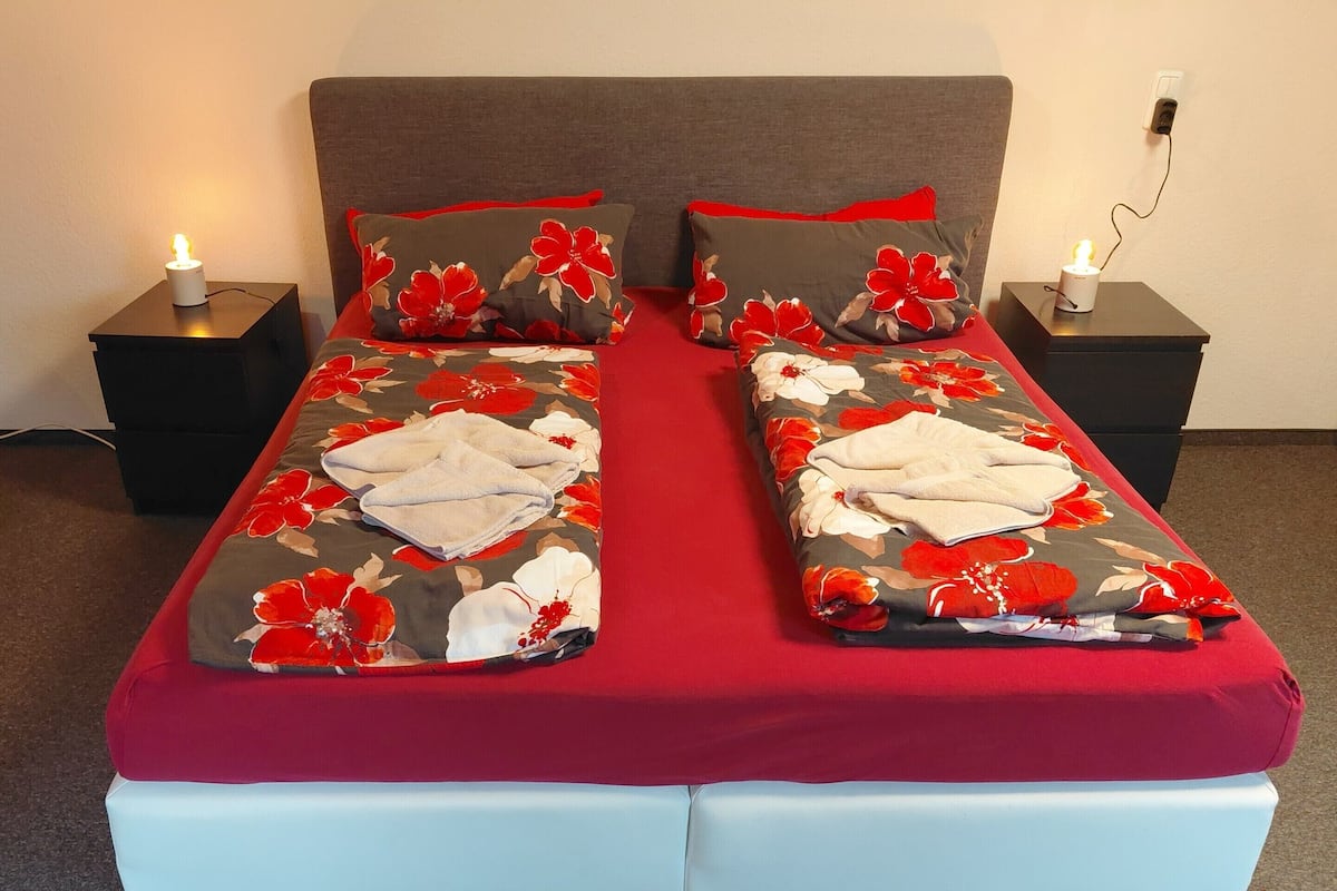 A double bed with floral bedding, two nightstands with candles, and a grey headboard.