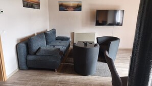 A modern living room with a sofa, a coffee table, and a TV mounted on the wall. - Pension Malu wo der Tag ab 6 Uhr mit einem guten Frühstück beginnt (Todenbüttel)