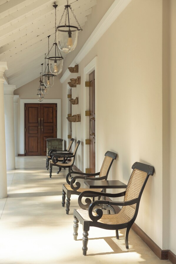 A hallway with wooden doors, wicker chairs, and hanging light fixtures.