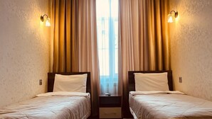 Une chambre d’hôtel avec deux lits simples, une table de chevet entre les deux et une fenêtre avec des rideaux.