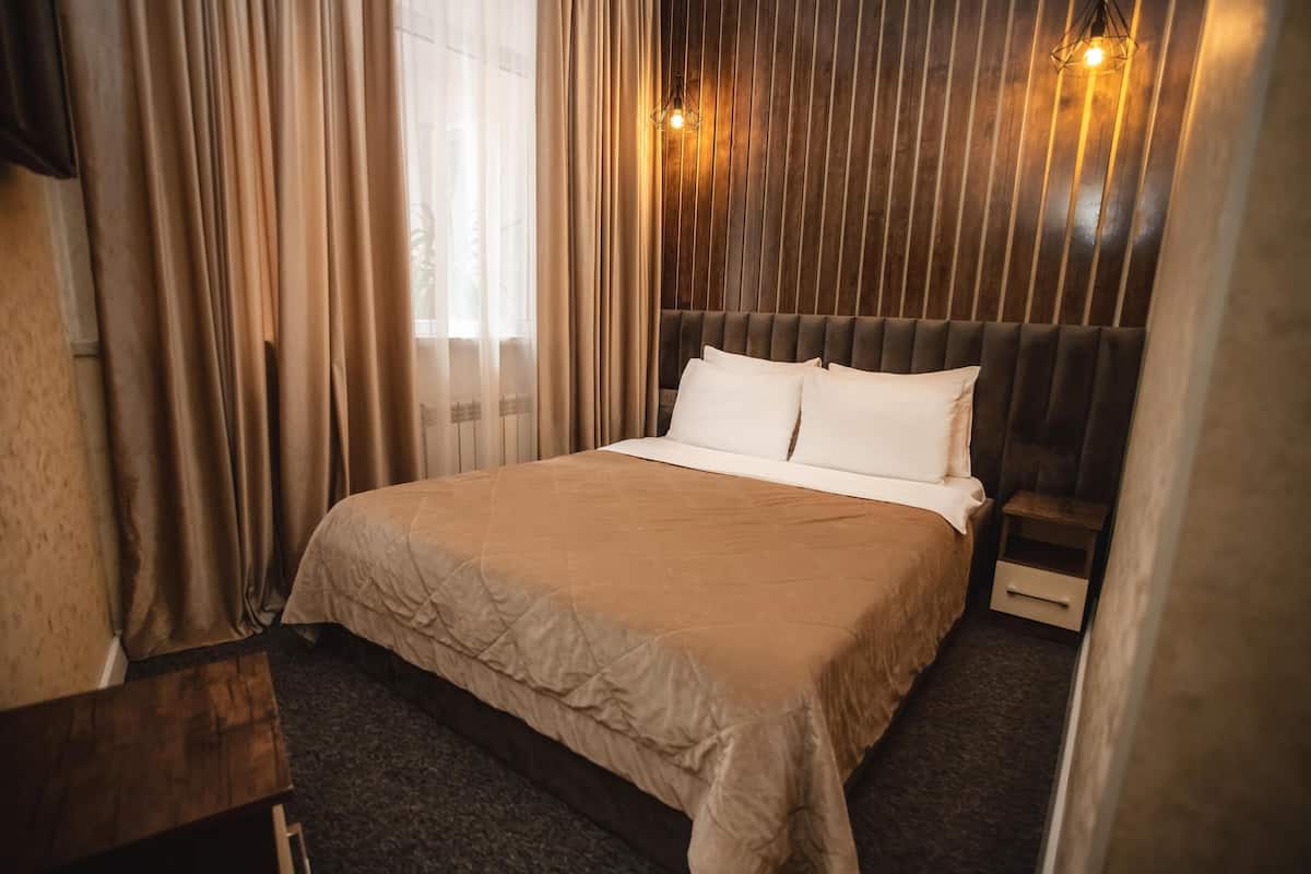 A neatly made bed with a beige bedspread, a wooden headboard, and a bedside table with a drawer.