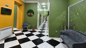 Un couloir avec un sol à carreaux noirs et blancs, des murs verts, un canapé gris, un radiateur et une plante.