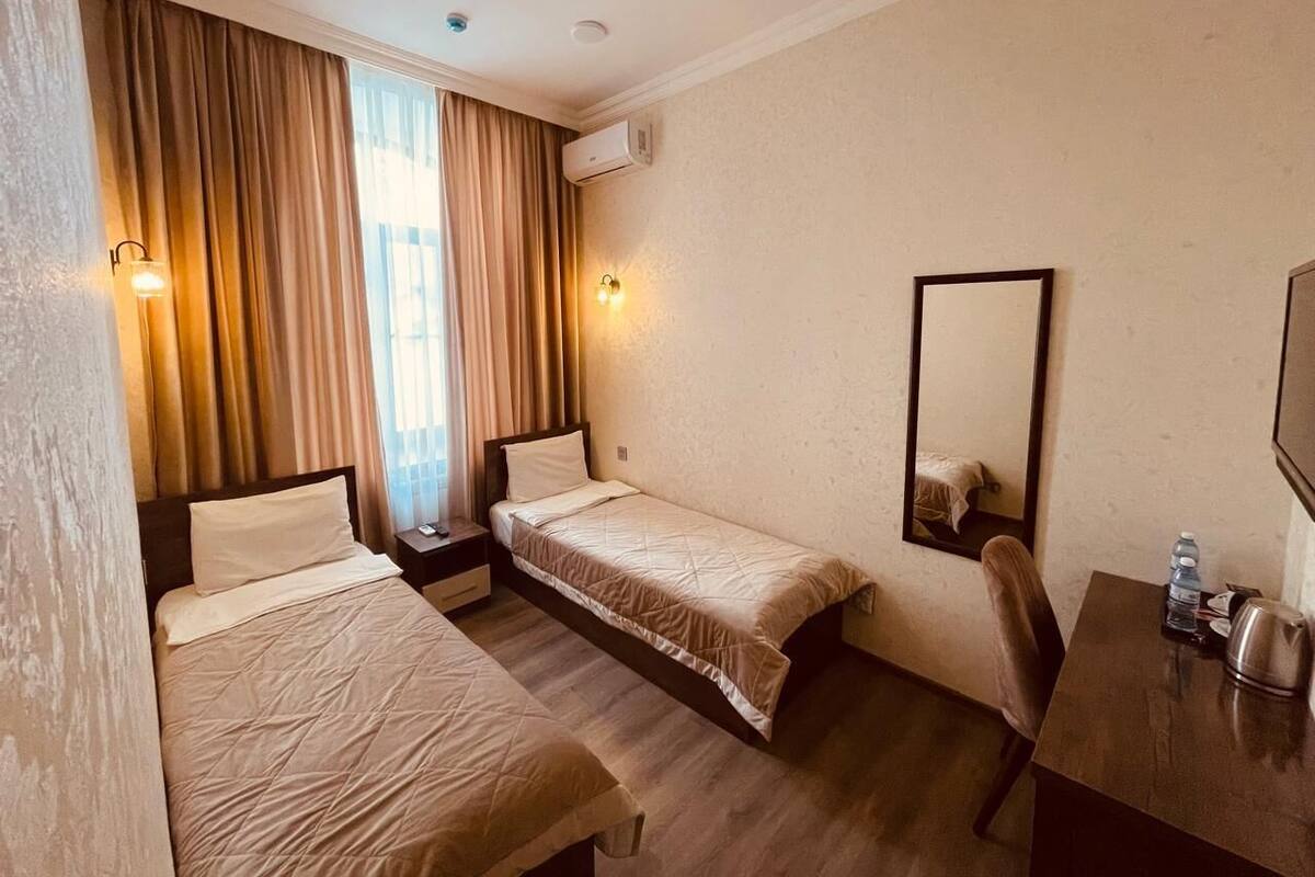 A hotel room with two single beds, a desk with a chair, a mirror, and a window with curtains.