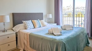 Un lit bien fait, avec une couvre-lit verte, des oreillers blancs et une tête de lit grise.