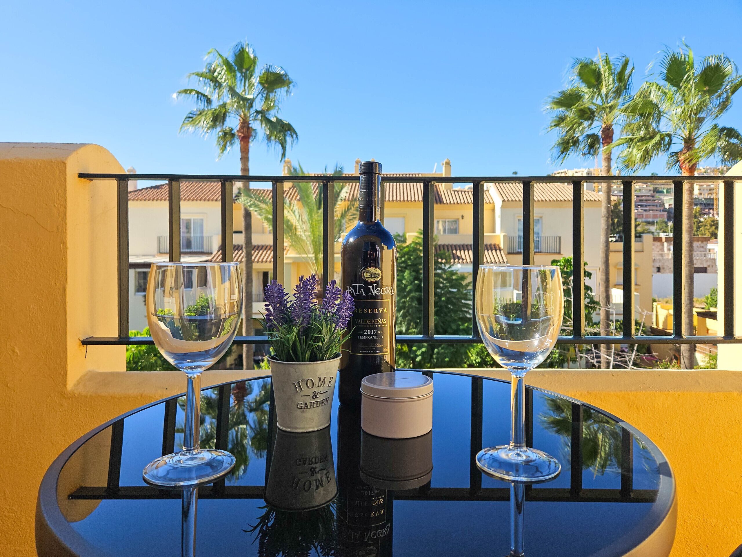 A balcony with a table set for two, featuring a bottle of wine, two glasses, and a potted plant.