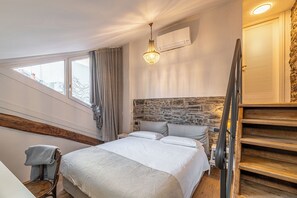 A bedroom with a bed, a stone wall, a wooden staircase, and a window with curtains. - Como Dreamhouse (Como)
