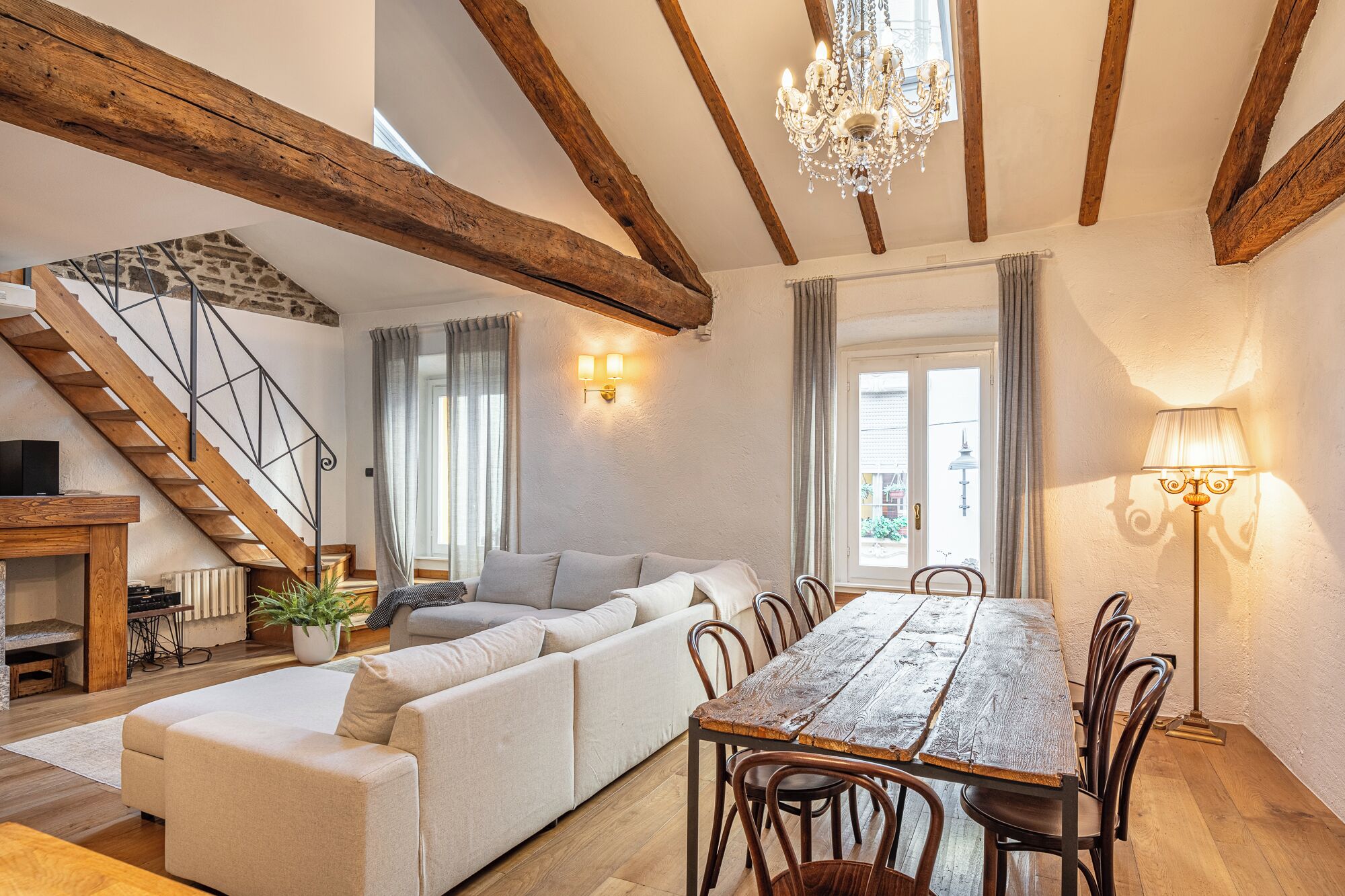 A spacious living area with a wooden dining table, a sofa, and a staircase.